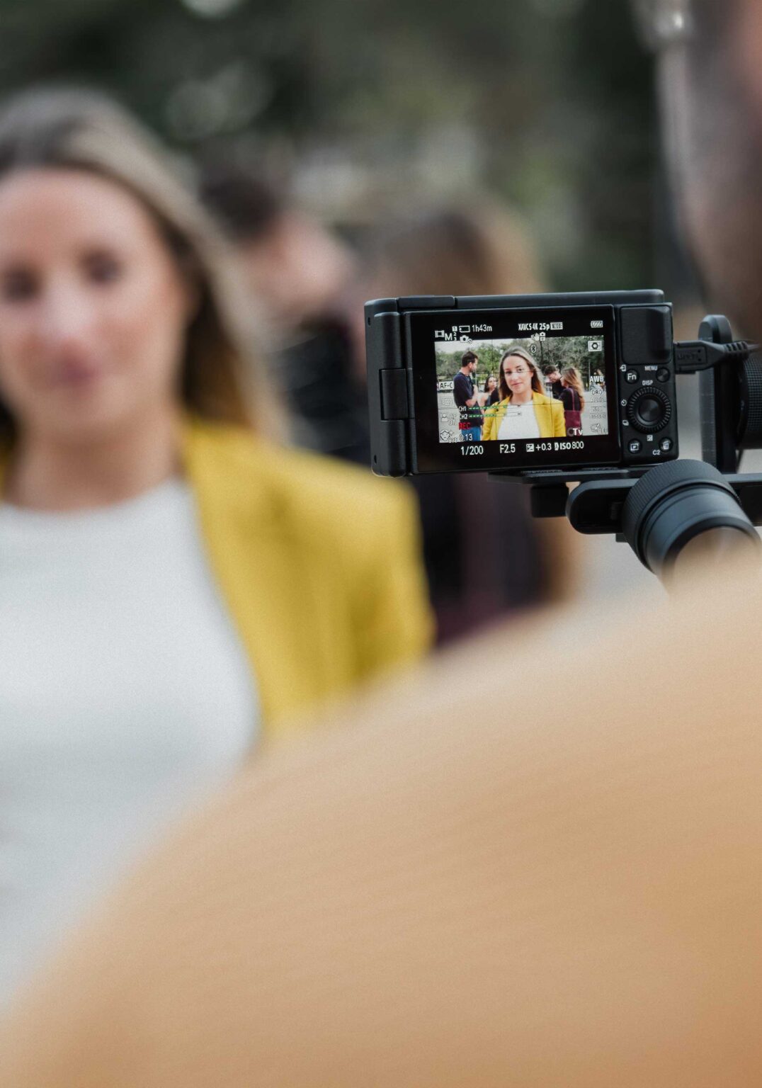 A man films a woman in a yellow jacket