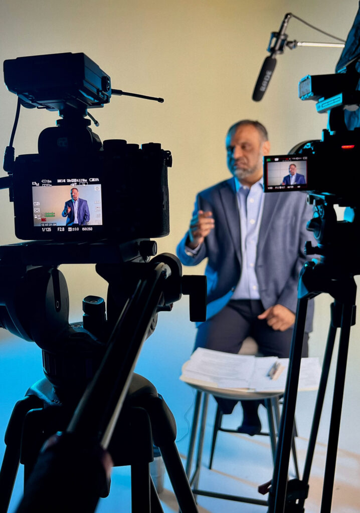 A man in a blue suit is being filmed by 2 cameras