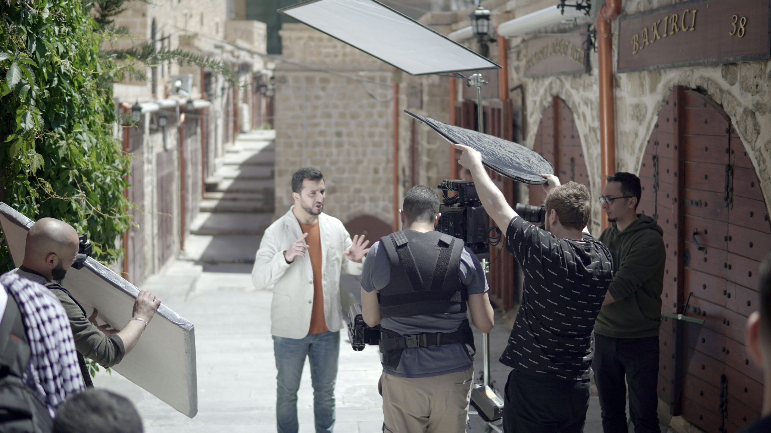 A man in a white jacket is being filmed in the street while singing