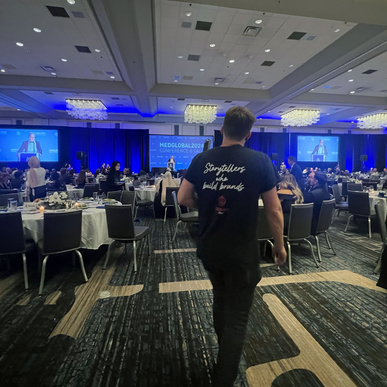 A man walks in front of a camera filming a stage